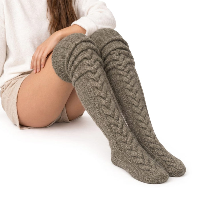 Personen bär långa, taupefärgade, kabelstickade Cozysocks som når över knäna.