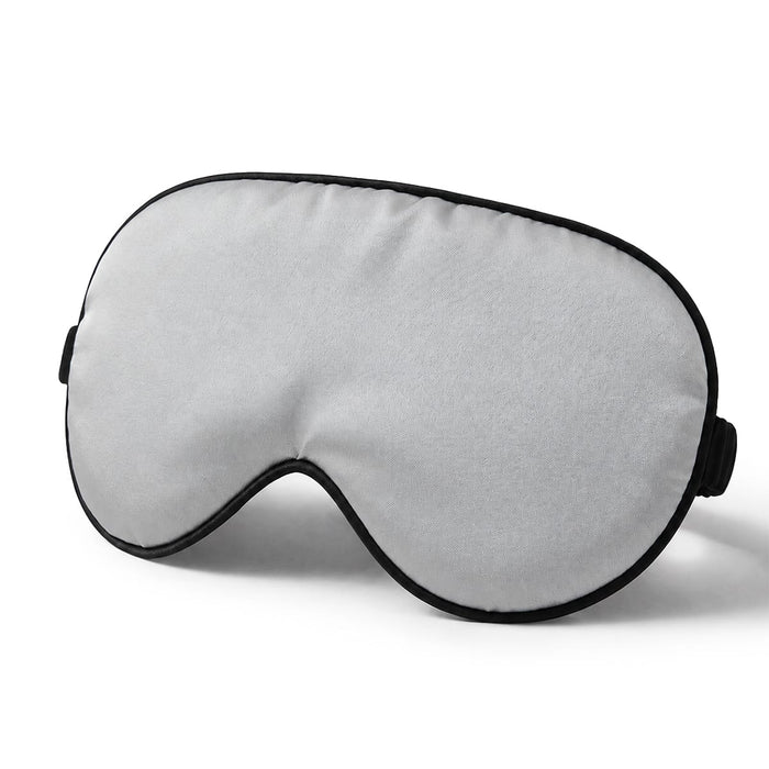 En ögonmask i silke i ljusgrått med svart kant och elastiskt band, avsedd för en bekväm sömn.