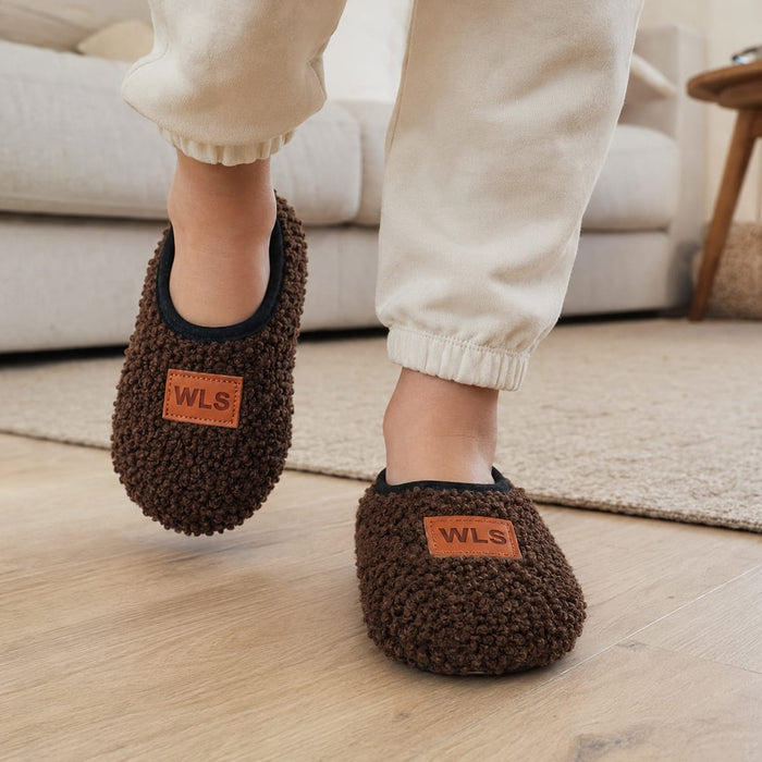 Barn bär halkfria inneskor på ett trägolv bredvid en beige soffa i butiken.