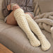 En person som sitter i en soffa och har på sig krämfärgade, kabelstickade Cozysocks-strumpor.