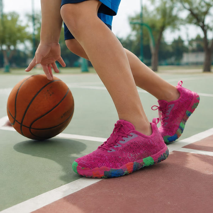 Barn dribblar basketboll utomhus iklädd rosa Barfotaskor Active med färgglada sulor.