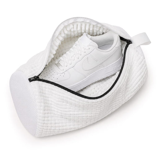 En vit sneaker placerad i en tvättpåse för skor, sedd uppifrån mot en enkel bakgrund.