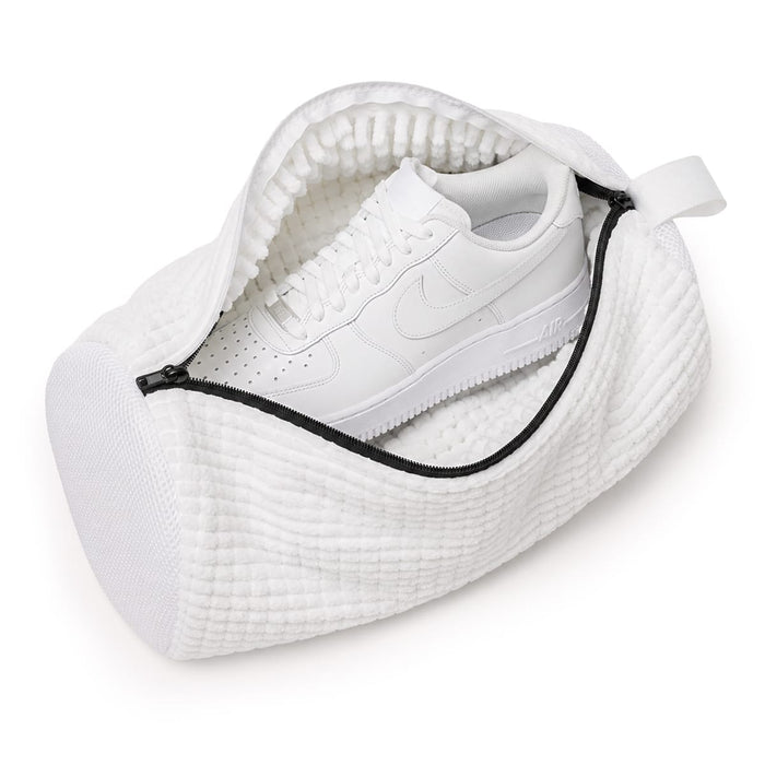 En vit sneaker placerad i en tvättpåse för skor, sedd uppifrån mot en enkel bakgrund.