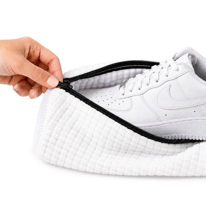 En hand lägger en vit sneaker i Kroppsbutikens tvättpåse för skor inför maskintvätt.