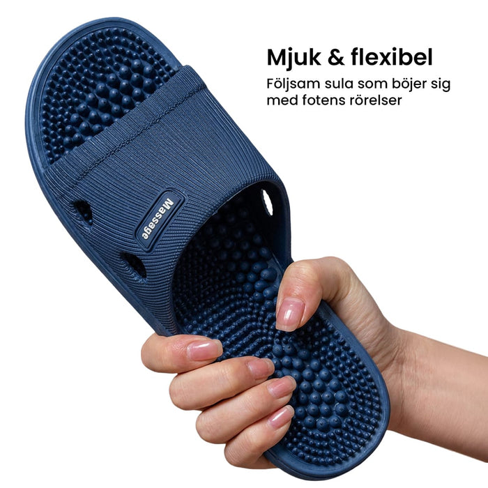 En hand håller ett par zonterapi-tofflor från Kroppsbutiken med en mjuk, flexibel sula och en upphöjd massageyta.