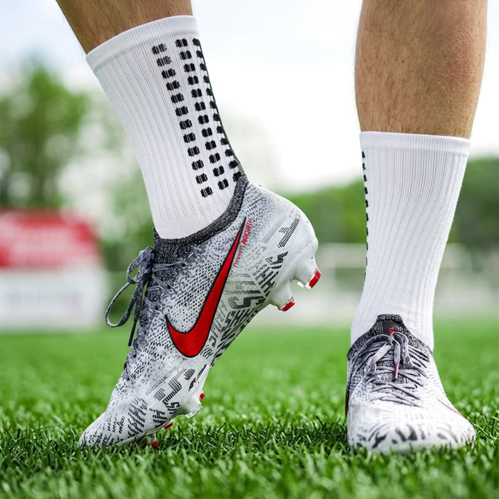 Närbild på fötter i vita Nike-fotbollsskor på gräs, med Kroppsbutikens halkskyddsstrumpor.