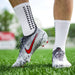 Närbild på fötter i vita Nike-fotbollsskor på gräs, med Kroppsbutikens halkskyddsstrumpor.