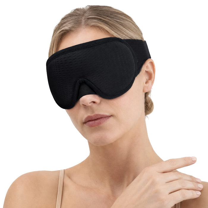 En kvinna med uppsatt hår och beige linne visar upp en 3D-sömnmask från Kroppsbutiken mot en vit bakgrund.