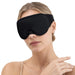 En kvinna med uppsatt hår och beige linne visar upp en 3D-sömnmask från Kroppsbutiken mot en vit bakgrund.