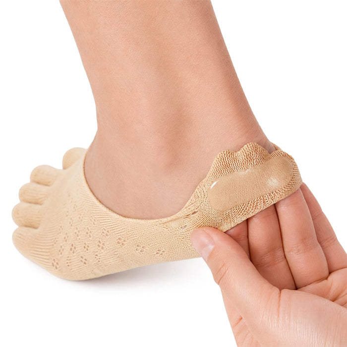 En hand drar upp en beige tåstrumpa med skydd för fotknölen på en fot där det sitter ett plåster mot skavsår på hälen.