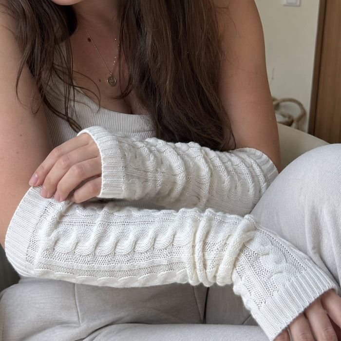 En kvinna med stickade handledsvärmare och en linne sitter avslappnat i soffan med armarna i kors.