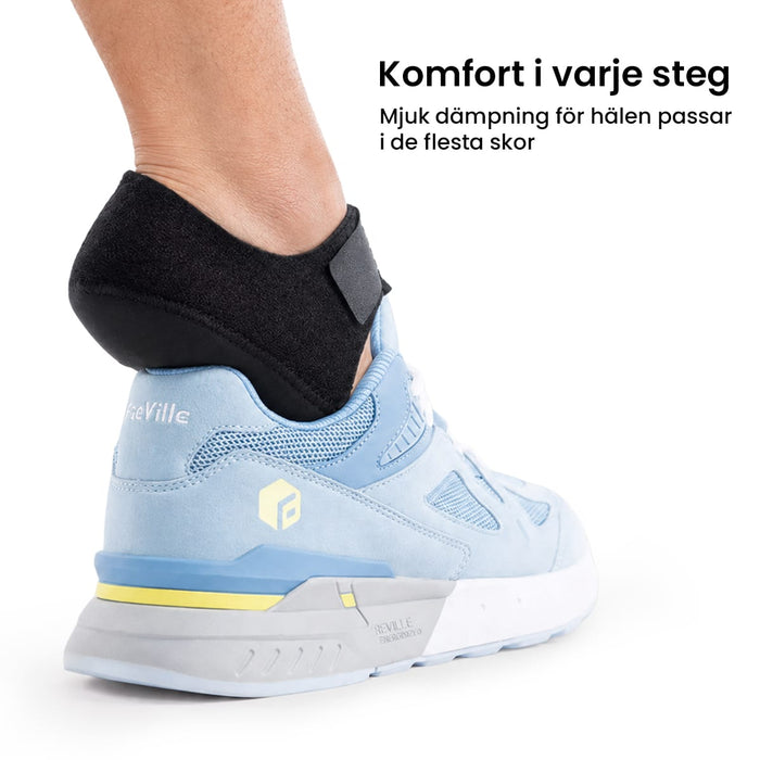 Person med en hälkudde från Kroppsbutiken mot hälsporre i ljusblå sneakers; på hälen syns en svensk text om hälkomfort.