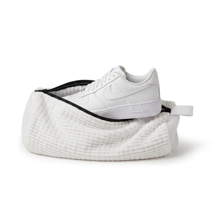 En vit sneaker ligger i en tvättpåse för skor från Kroppsbutiken, fotograferad mot en vit bakgrund.