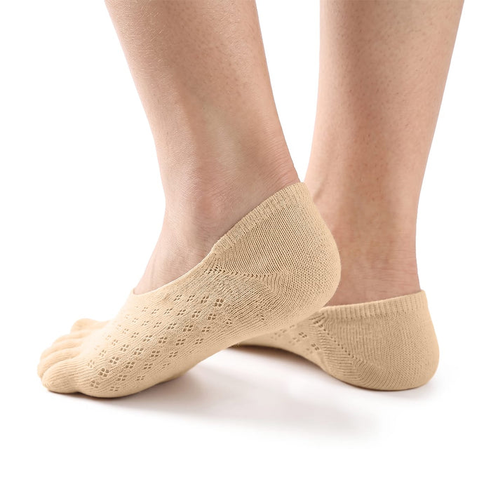 En person bär beige tåstrumpor med stöd för hallux valgus och mönster, stående mot en vit bakgrund.