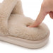 Ett finger trycker mot den mjuka, beige ytan på en vintertoffel från Kroppsbutiken mot en vit bakgrund.